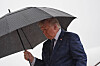 Donald Trump går utendørs under en paraply i regnvær ved et fly.