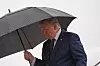 Donald Trump går utendørs under en paraply i regnvær ved et fly.