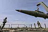 To soldater håndterer en stor rakett med kran på en åpen militærbase.