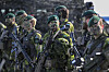 Svenske soldater i kamuflasje og grønne bereter står bevæpnet under en militærøvelse utendørs.