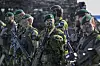 Svenske soldater i kamuflasje og grønne bereter står bevæpnet under en militærøvelse utendørs.