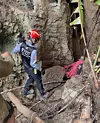 Redningsarbeider med hjelm og tau ved smal huleinngang i bratt terreng
