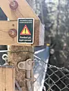 Nærbilde av advarselsskilt på trekonstruksjon ved en smal hengebru i skogsterreng.