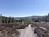 Smalt grusspor gjennom åpent skogsterreng med innsjø og åser i bakgrunnen.