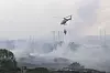 Brannhelikopter slipper vann over røykfylt landskap på Sotra i Øygarden.