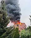 Store flammer og svart røyk stiger fra taket på et leilighetsbygg omgitt av trær.