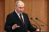 Putin står ved en talerstol med mikrofoner og gestikulerer under en tale innendørs.