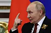 Vladimir Putin gestikulerer mens han snakker foran russiske flagg i en sal i Kreml.