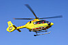 Gul luftambulansehelikopter i lufta mot blå himmel.