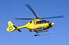Gul luftambulansehelikopter i lufta mot blå himmel.