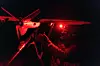 Soldat i mørke justerer en drone opplyst av rødt lys på et stativ.