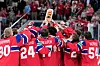 Norske ishockeyspillere i røde drakter løfter bronsetroféet foran publikum.
