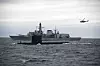 Svensk ubåt på sjøen med et britisk skip og et helikopter i bakgrunnen.