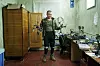 Ukrainsk soldat holder to FPV-droner i et lite, slitt verkstedrom med utstyr og deler på bordene.