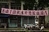Beboere spiller kort under et rosa banner med myggkontrollbudskap ved et boligkompleks i Guangzhou.