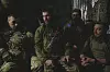 Fire bevæpnede soldater sitter sammen i en mørk skyttergrav med grønt militært utstyr.