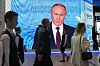 Flere personer går forbi en stor skjerm som viser et portrett av Vladimir Putin på et økonomiforum.