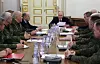 Vladimir Putin sitter ved enden av et langt møtebord omgitt av militære offiserer i en sal med hvite og gullfargede vegger.