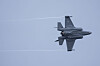 En grå F-35-jager flyr mot blå himmel med kondensstriper bak.