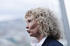 Kvinne med krøllete blondt hår i profil mot lys bakgrunn.