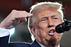 Donald Trump taler inn i en mikrofon med hånden løftet i en utendørs scene.