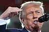 Donald Trump taler inn i en mikrofon med hånden løftet i en utendørs scene.