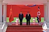 To menn og to barn står på en opphøyd scene med rødt bakteppe og flagg fra Nord-Korea og Kina.