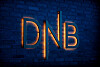 Gult DNB-logo skinner på en blå mursteinsvegg i mørkt lys.