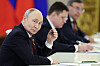 Vladimir Putin sitter ved et møtebord og holder en penn mens en annen mann sitter uklart i bakgrunnen.