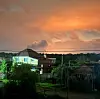 Hus og trær i et boligområde under en oransje himmel ved solnedgang.