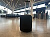 En svart kabinkoffert står på et tregulv i en tom flyplassterminal.