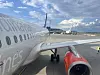 Utsikt fra et fly med motor og vinge mot en flyplassrullebane og terminalbygninger i bakgrunnen.
