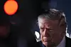Donald Trump står i profil i mørket med lys fra flyplassen bak, før han går om bord i et fly.