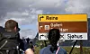 Turister står ved skilt til Reinebringen ved en sti i Reine i Lofoten.