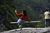 Turister sitter og står ved et utsiktspunkt i Geiranger med fjellandskap i bakgrunnen.