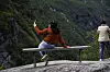 Turister sitter og står ved et utsiktspunkt i Geiranger med fjellandskap i bakgrunnen.