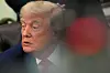 President Donald Trump sits in the Oval Office, seen through a blurred foreground.