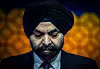 Nærbilde av en mann i mørk dress og turban foran en varm, oransje bakgrunn.