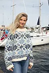 En kvinne står foran en båt i en marina og har på seg en blå og hvit mønsterstrikket genser.