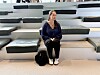 En kvinne sitter på trappetrinn i et lyst amfirom med en veske ved siden av seg.