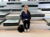 En kvinne sitter på trappetrinn i et lyst amfirom med en veske ved siden av seg.