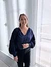 Smilende kvinne står foran store vinduer i et lyst rom.