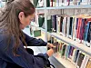 En kvinne sitter ved en bokhylle og trekker ut en bok på et bibliotek.