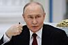 Vladimir Putin sitter ved et bord og holder en hånd nær ansiktet under et møte innendørs.