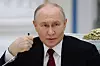 Vladimir Putin sitter ved et bord og holder en hånd nær ansiktet under et møte innendørs.