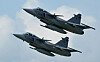 To grå JAS 39 Gripen-jagerfly flyr tett sammen mot en lys himmel.