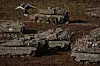 Flere stridsvogner og militære kjøretøy står parkert på et jordet område med soldater rundt.