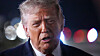 Nærbilde av Donald Trump foran uskarpe lys mens han snakker utendørs om kvelden.