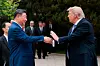 Donald Trump og Xi Jinping håndhilser utendørs med flere menn stående bak dem.