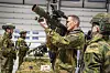 En soldat holder opp et bærbart luftvernsystem innendørs mens andre soldater står i bakgrunnen i kamuflasjeuniformer.